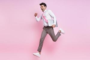 Excited young man in shirt and tie jumping against pink background photo