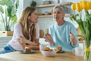 Senior mother and her adult daughter communicating while enjoying sweet food at the kitchen photo