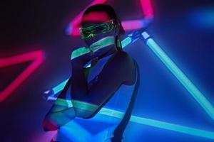 Young woman in futuristic glasses standing against colorful background photo