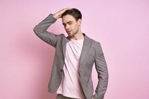 Handsome young man in suit holding hand in hair while standing against pink background photo