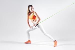 Beautiful woman in sports clothing using resistance band while exercising against white background photo