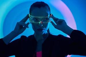 Confident young woman adjusting futuristic glasses against colorful background photo