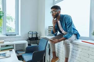 Thoughtful young man holding digital tablet while sitting on the window sill photo