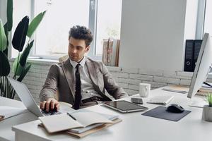 apuesto joven usando computadora mientras está sentado en su lugar de trabajo en la oficina foto