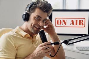 un joven apuesto que usa el micrófono mientras graba un podcast en el estudio foto