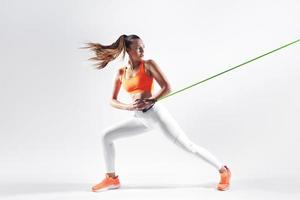 Confident young woman using resistance band while exercising against white background photo