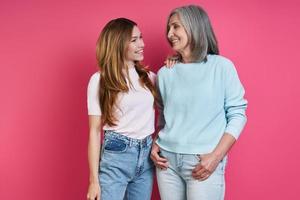 Happy mother and adult daughter standing together against pink background photo