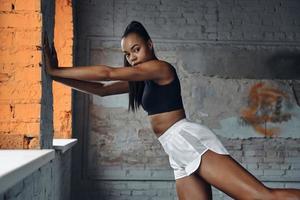 Confident young African woman in sports clothing doing stretching exercises in gym photo