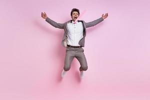 Excited young man in full suit jumping against pink background photo