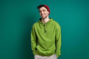 Confident young man looking at camera and smiling while standing against green background photo