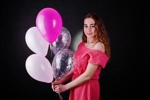 Young girl in red dress with balloons against black background on studio. photo