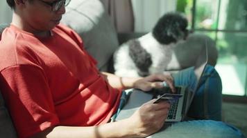 homem de negócios segurando cartão de crédito usando computador portátil para pagamento fácil on-line através de aplicativo de banco eletrônico sentado no sofá no escritório em casa. tecnologia de internet e transação financeira sem fio video