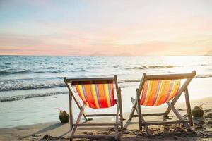 Couple relax chair on sand beach with warm sunset - vacation in beautiful sea nature concept photo