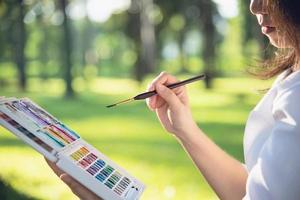 Relax woman painting water colour art work in green garden forest nature - people with creative art in nature stress reduction and meditation concept