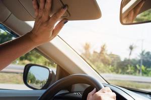 la señora ajusta la visera mientras conduce el automóvil en la carretera - automóvil interior usando el concepto foto