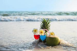 Cocktail glasses with coconut and pineapple on clean sand beach - fruit and drink on sea beach backgroudn concept photo