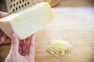 Woman preparing cheese for cook using cheese grater in the kitchen - people making food with cheese concept photo