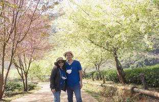 Asian couple happy taking photo in beauliful nature Prunus cerasoides Sakura of Thailand flower garden in Doi Ang Khang, Chiangmai Thailand