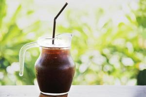 Ice coffee on wooden table over green garden background - relax with beverage in nature concept photo