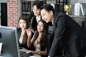 successful business multiage team standing around computer for presentation of work. Group of business people in a meeting at office, working on computer photo