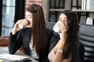 descanso para tomar café en la oficina con dos colegas sentadas charlando con tazas de café. mujer de negocios asiática sosteniendo una taza de café en la oficina. foto