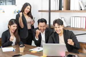 gente de negocios feliz en la computadora celebrando el éxito en el trabajo sentado en la oficina moderna. negociaciones exitosas. equipo de negocios mirando el monitor de la computadora. foto