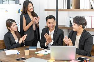 Happy business team applauding. Business people working together on project and brainstorming in office. Friendly diverse employees congratulating businesswoman with business achievement. photo