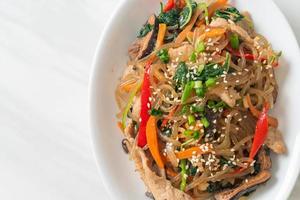 japchae or stir-fried Korean vermicelli noodles with vegetables and pork topped with white sesame photo