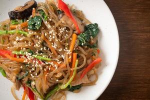 japchae or stir-fried Korean vermicelli noodles with vegetables and pork topped with white sesame photo