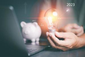 young man holding a light bulb in his hand And there is a graph showing the growth of savings in 2023. Finance and investment ideas. and income planning from the profits of the business photo