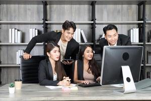 exitoso equipo empresarial multiedad de pie alrededor de la computadora para la presentación del trabajo. grupo de empresarios en una reunión en la oficina, trabajando en la computadora foto