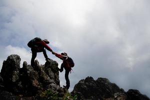 Person hike friends helping each other up a mountain. Man and woman giving a helping hand and active fit lifestyle. Asia couple hiking help each other. concept of friendship, teamwork. photo