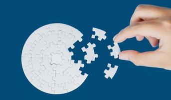 Close up hand holding and playing jigsaw game incomplete. White part of jigsaw puzzle pieces on blue background. concepts of problem solving, business, teamwork, Texture photo with copy space for text