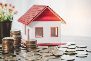 modelo de casa y pilas de monedas de dinero en el fondo de la mesa borrosa. planes de ahorro para vivienda, préstamo, inversión, hipoteca, finanzas y banca sobre el concepto de casa. foto