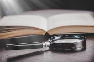 open book with magnifying glass on wooden desk in information library of school or university, concept for education,reading , study, copy space on table background. photo