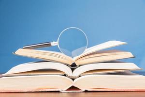 open book with magnifying glass on wooden desk in information library of school or university, concept for education,reading , study, copy space and blue background. photo