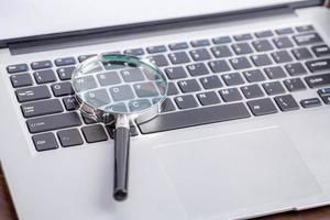 Laptop computer keyboard with magnifying glass, concept of search photo