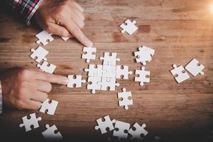 Hands holding jigsaw puzzles piece on wooden table background, success business, solution strategy, teamwork partnership concept