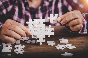 Hands holding jigsaw puzzles piece on wooden table background, success business, solution strategy, teamwork partnership concept photo