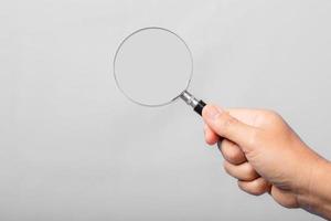 woman hand holding magnifying glass isolated on gray background. optical zoom lens is macro tool, concept for education, science. photo