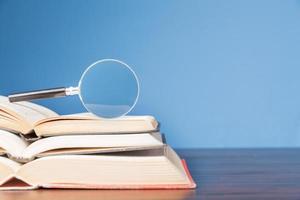 open book with magnifying glass on wooden desk in information library of school or university, concept for education,reading , study, copy space and blue background. photo