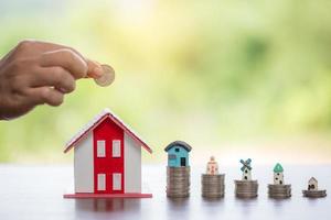 Hand putting coin in house model of coin for saving money for buying house. Savings plans for home, loan, investment, mortgage, finance and banking about house concept. photo