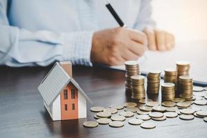 modelo de casa con monedas apiladas, la mano de negocios está planeando ahorrar dinero en monedas para comprar una casa. concepto de escalera de propiedad, hipoteca con inversión inmobiliaria y ahorro o inversión para una casa foto