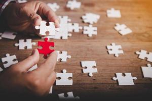 Hands holding jigsaw puzzles piece on wooden table background, success business, solution strategy, teamwork partnership concept photo