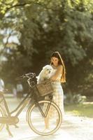 mujer joven con perro bichon frise blanco en la cesta de la bicicleta eléctrica foto