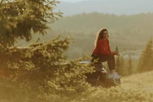 Young woman relaxing on a terrain vehicle hood at countryside photo