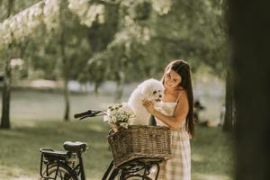 mujer joven con perro bichon frise blanco en la cesta de la bicicleta eléctrica foto