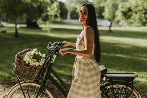 mujer joven con bicicleta eléctrica y flores en la cesta foto