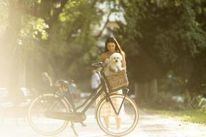 mujer joven con perro bichon frise blanco en la cesta de la bicicleta eléctrica foto