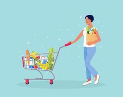 Woman with paper bag pushing shopping cart full of groceries in the supermarket. There is a bread, bottles of water, milk, fruits, vegetables and other products in the basket vector